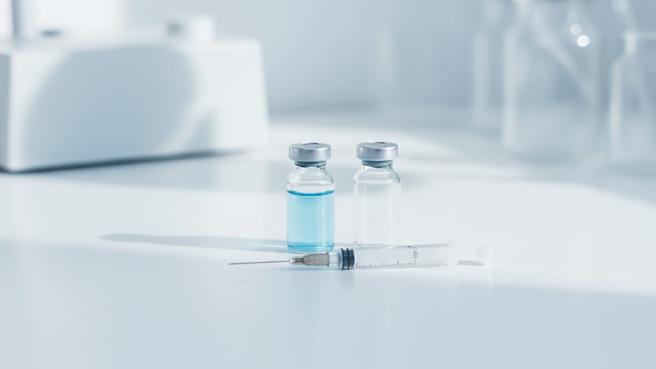 Illustration: A clear glass vial with pale blue liquid, an empty vial, and an insulin syringe on a white surface.