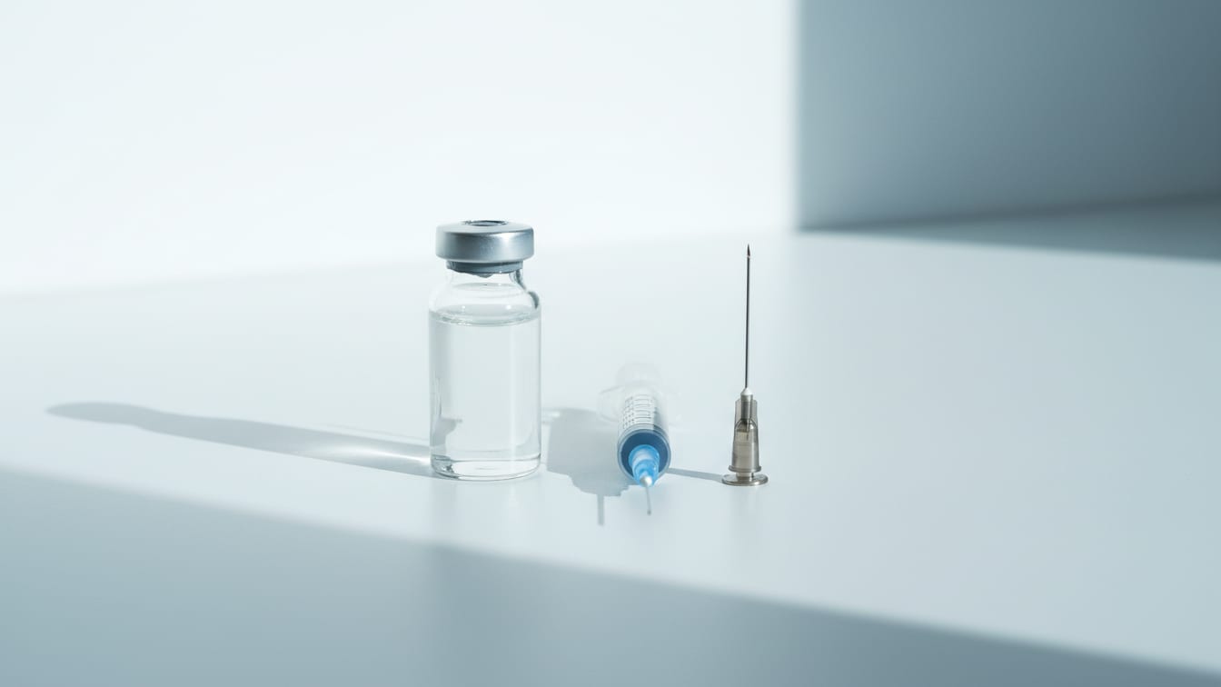 Illustration: A clear glass vial of water and an insulin syringe lie parallel on a white bench.
