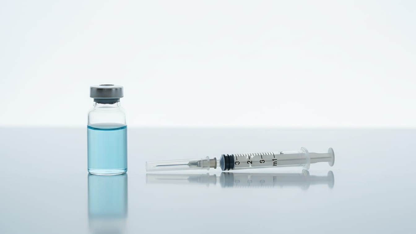 Illustration: A clear glass vial with pale blue liquid and an insulin syringe on a white surface.