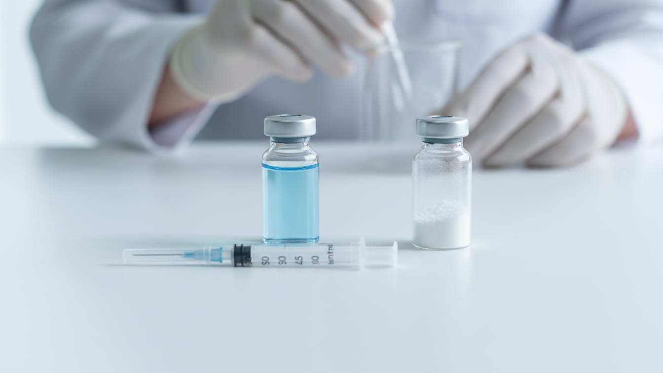 Illustration: A partially filled vial and an empty lyophilized vial with an insulin syringe on a white surface.
